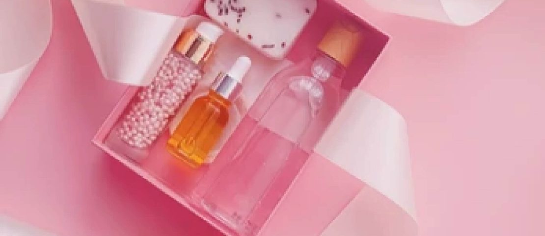 pink subscription box filled with beauty products surrounded by a pink ribbon on a pink background